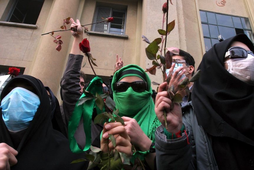 Women wearing green or black Islamic veils hold roses