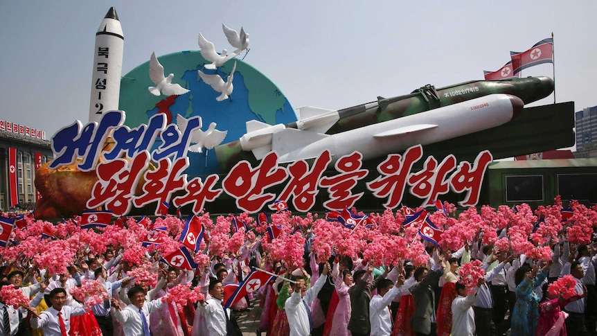 North Koreans march next to a float adorned with different models of missiles, half a globe of the earth and white doves.