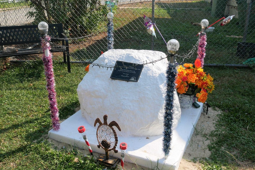 A large white rock sits in the front yard of a house, decorated with tinsel poles, lights, flowers