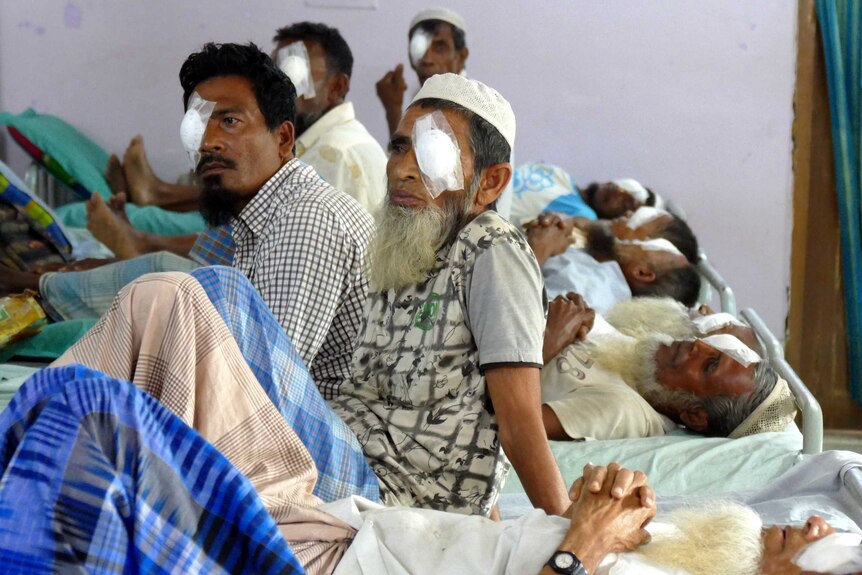 A group of men sit and lie down with surgical patches over their eyes