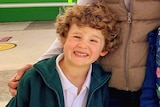A young boy with curly hair, smiles.