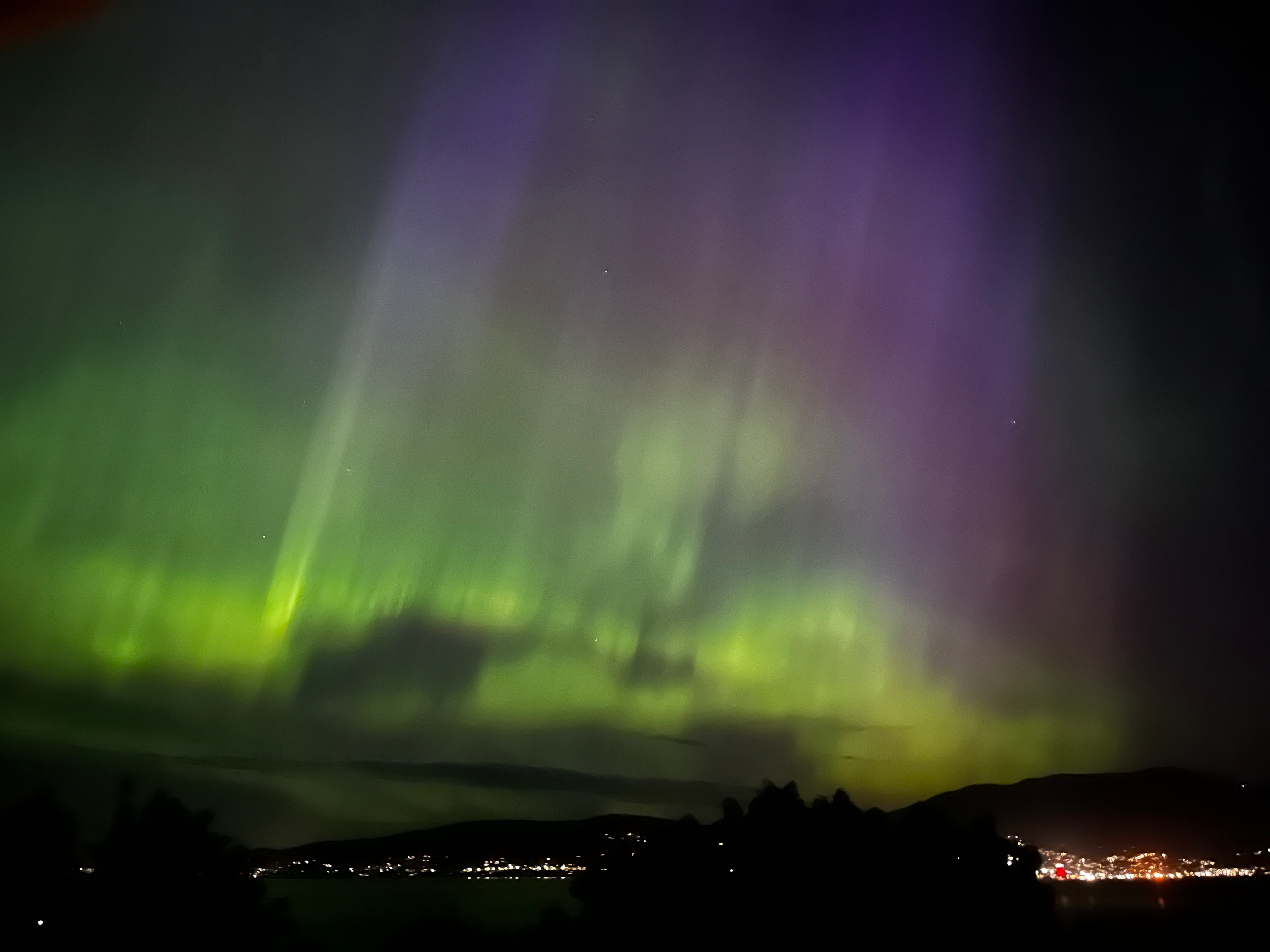 Luces brillantes verdes y violetas en el cielo sobre las luces de la ciudad.