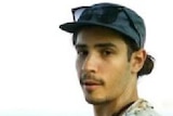 A photo of a young man wearing a hat with his sunglasses on it, and a floral shirt.