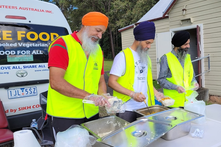 Three men volunteering for Sikh Volunteers Australia, serving food alongside the organisation's van. 