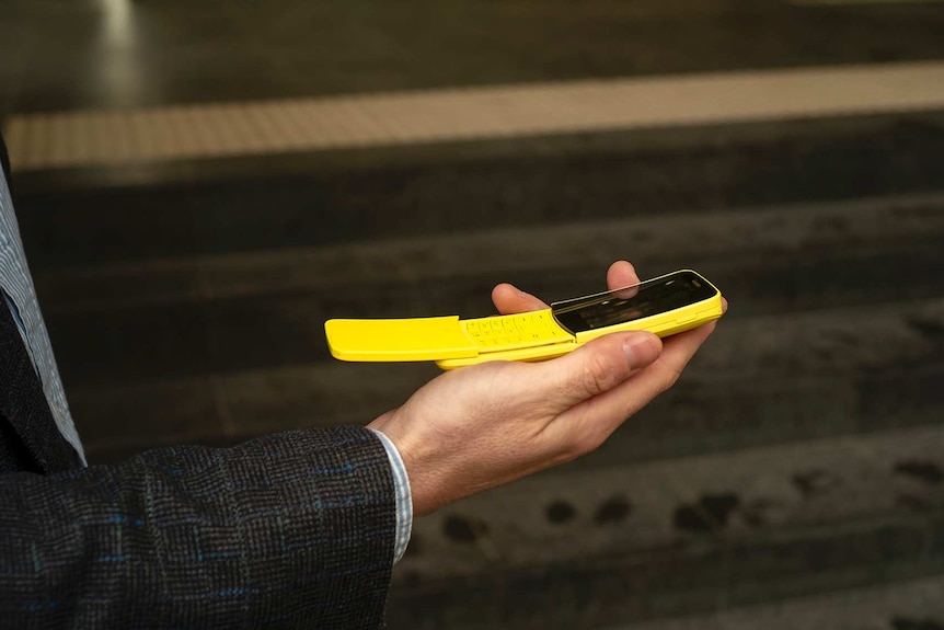 A close-up of a man holding a yellow flip phone.