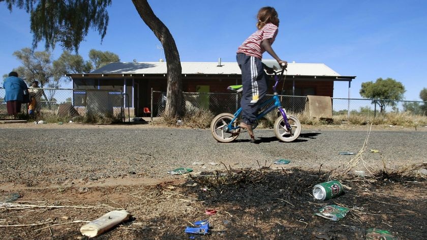 A child rides a bike through an Aboriginal camp.