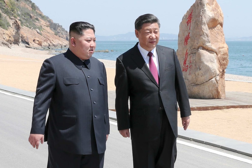 Kim Jong-un walks next to Xi Jinping with a beach in the background.