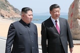 Kim Jong-un walks next to Xi Jinping with a beach in the background.