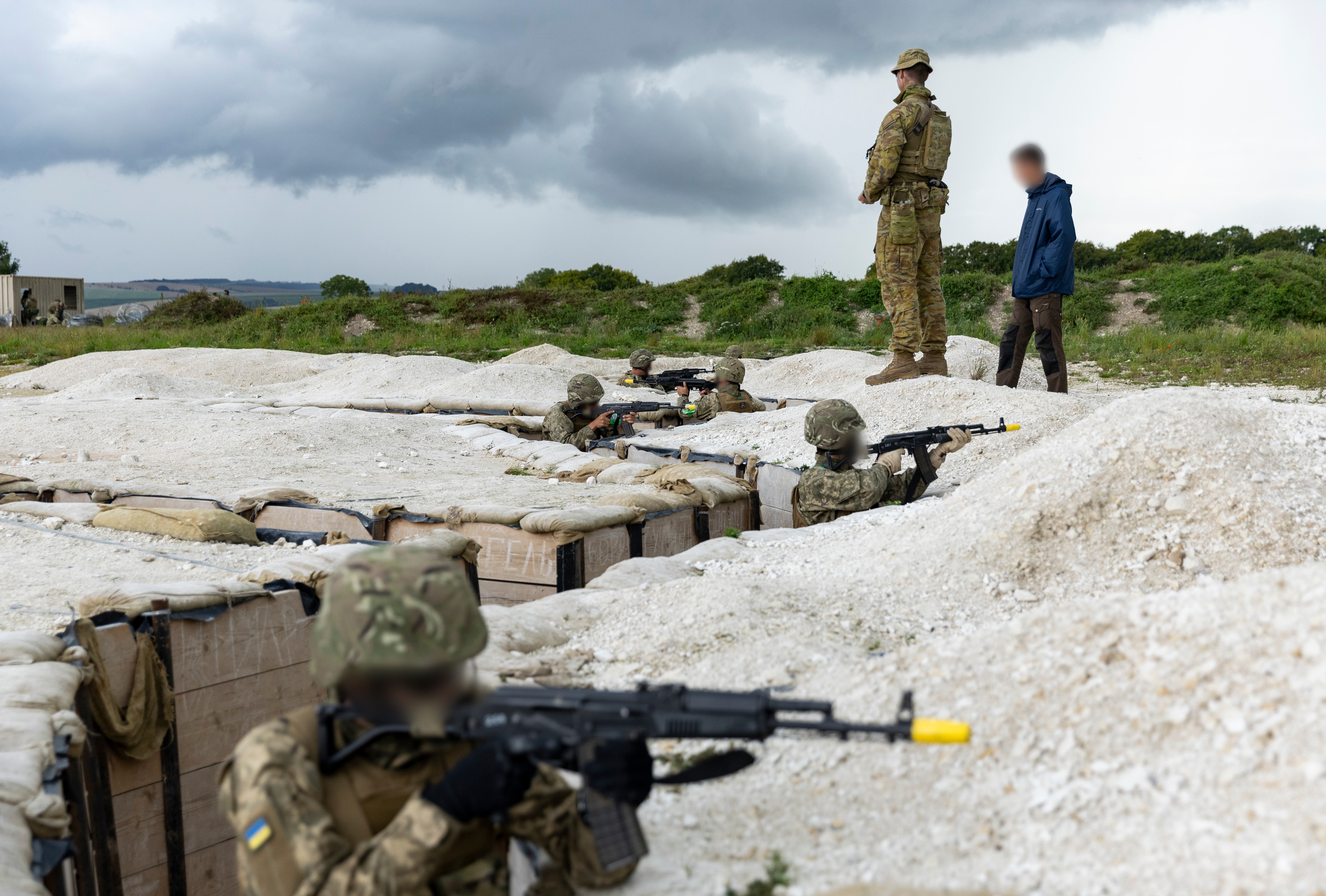 Several people in camouflaged gear sit in trenches.