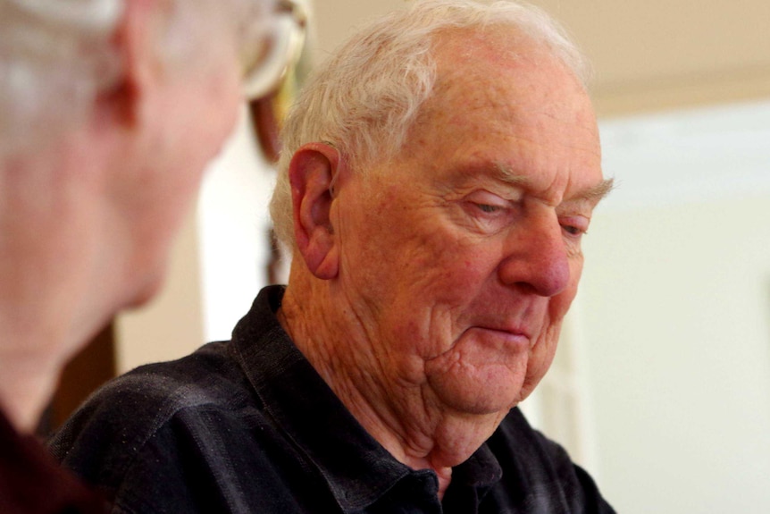 An elderly man wearing a black shirt sitting at a kitchen table