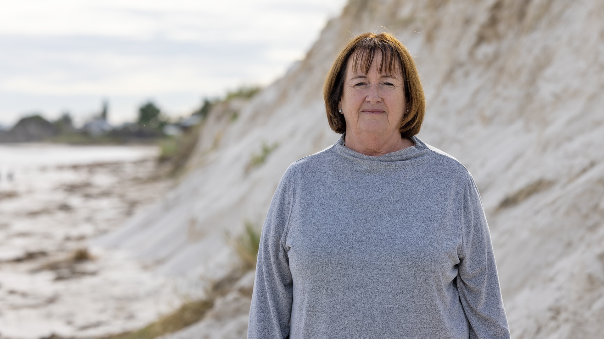Linda Balcombe standing in front of an eroded sand dune, frowning 