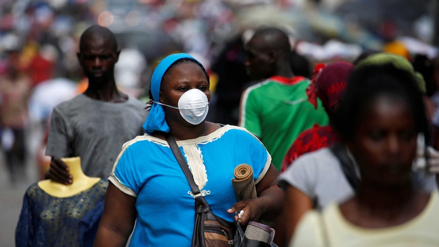 A woman wears a protective mask as she walks down the street holding bags.