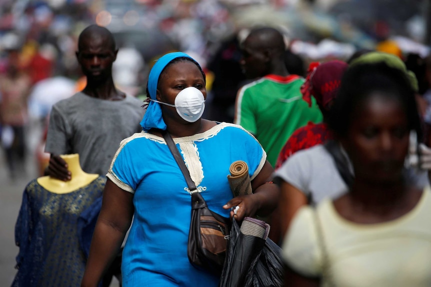 A woman wears a protective mask as she walks down the street holding bags.