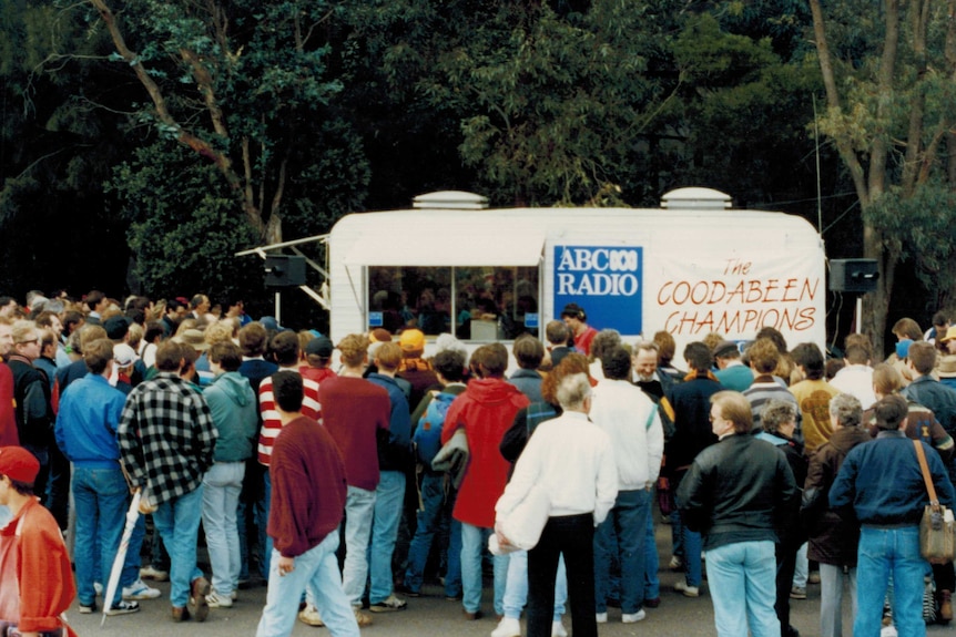 ABC Radio caravan with Coodabeen Champions sign surrounded by large crowd.