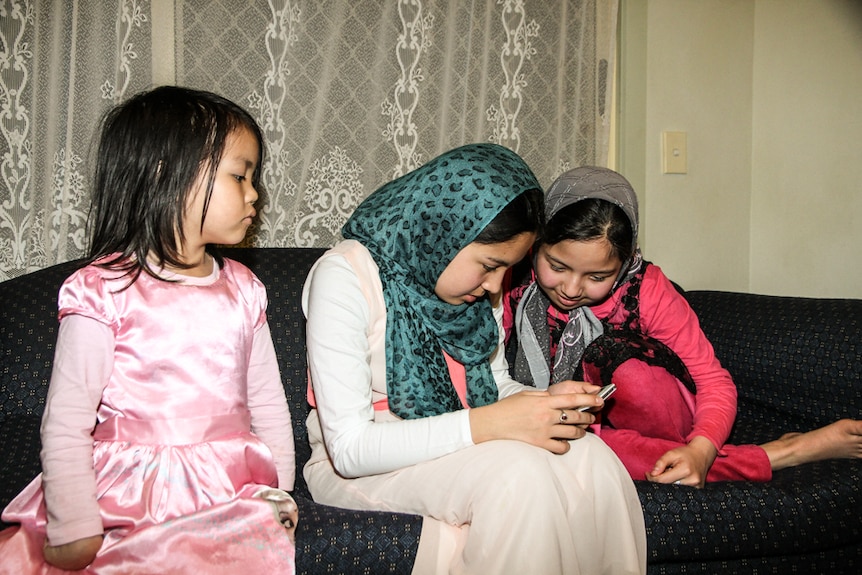 14-year-old Zahra Azimi on the phone with her 12-year-old sister Masoomeh (right) and six-year-old Simara gul Babaali looking on