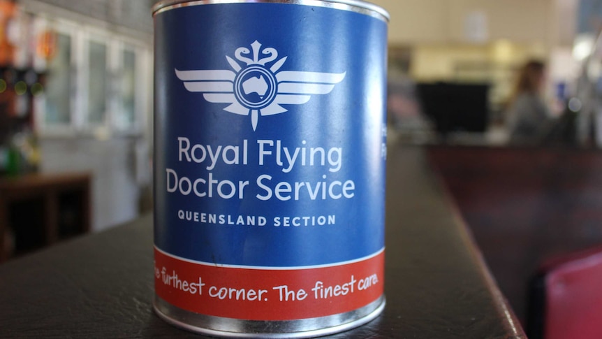 A blue donation tin with a red band sits on a shop counter. It reads 'Royal Flying Doctor Service.'