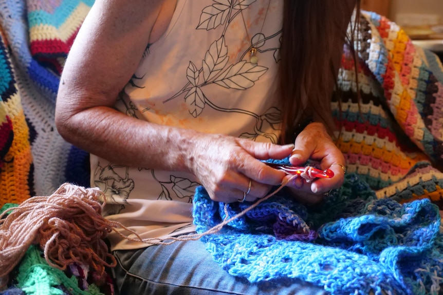 A woman's hands making a blue crochet blanket.