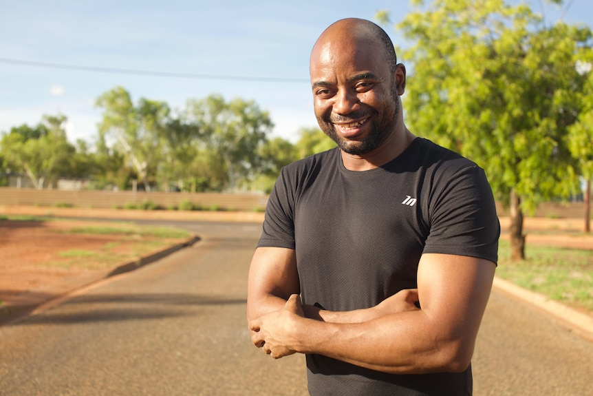 Marcel smiles while crossing his arms as he stands on a street.