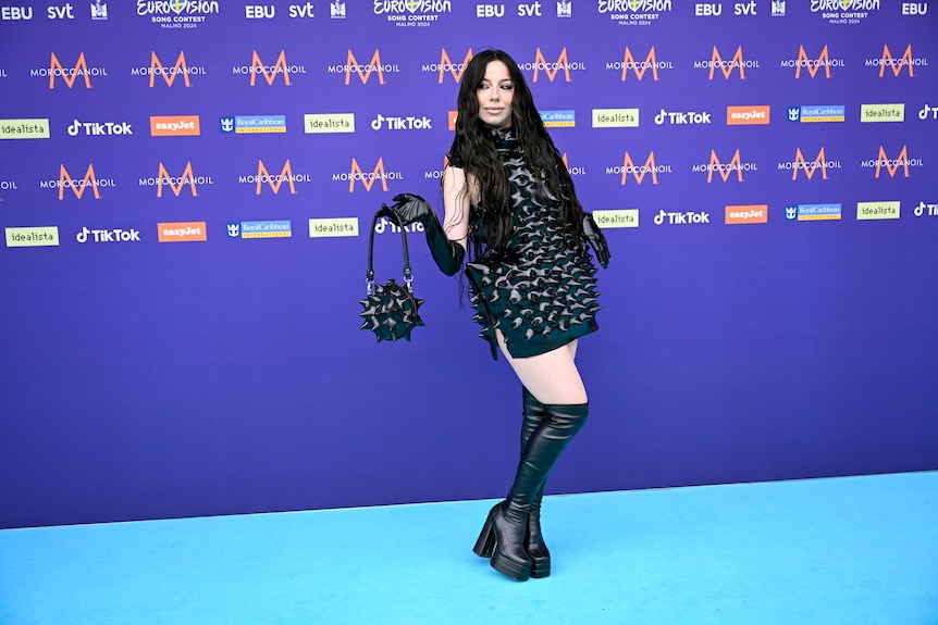 Sarah Bonnici wearing black plasic inflatable-looking mini dress with spikes and a handbag that looks like a medieval weapon