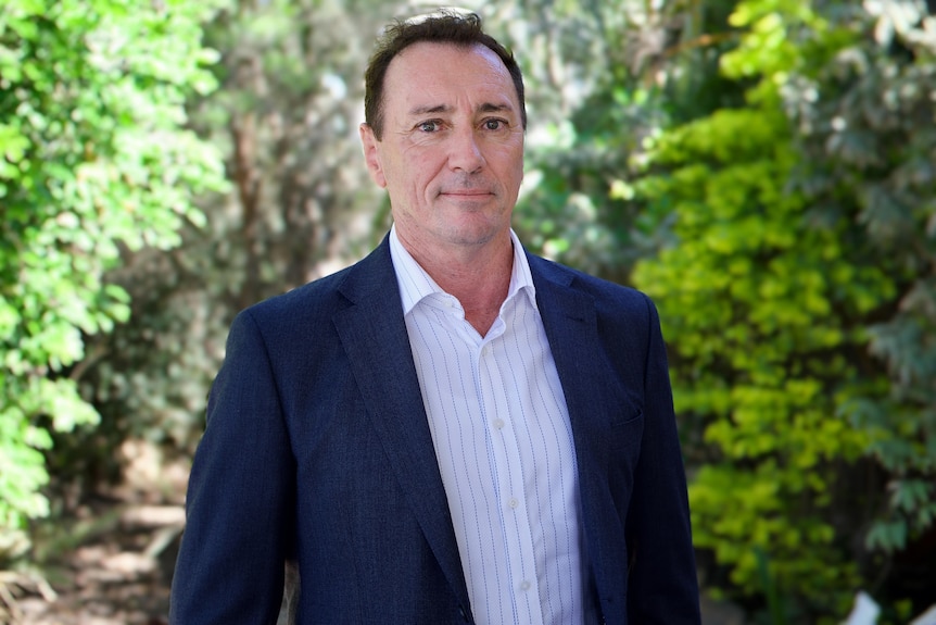 Steve Griffiths standing in a blue suit with a green background. 