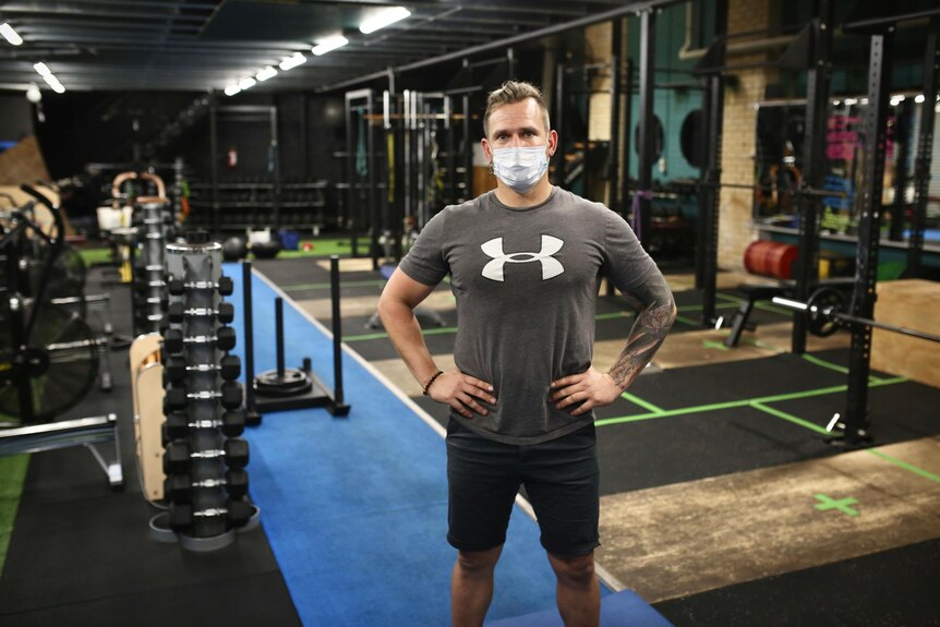 A man with a face mask stands in an empty gym