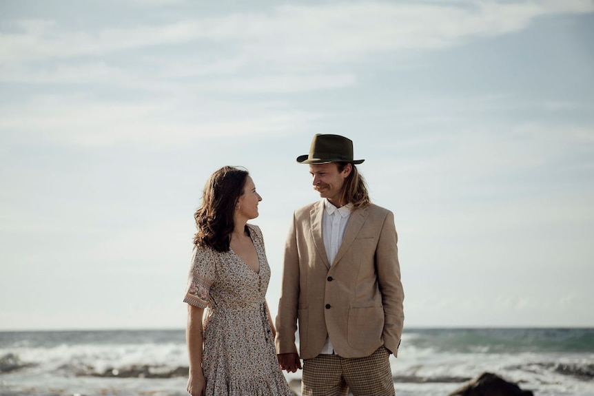 A couple gaze at each other on a beach.