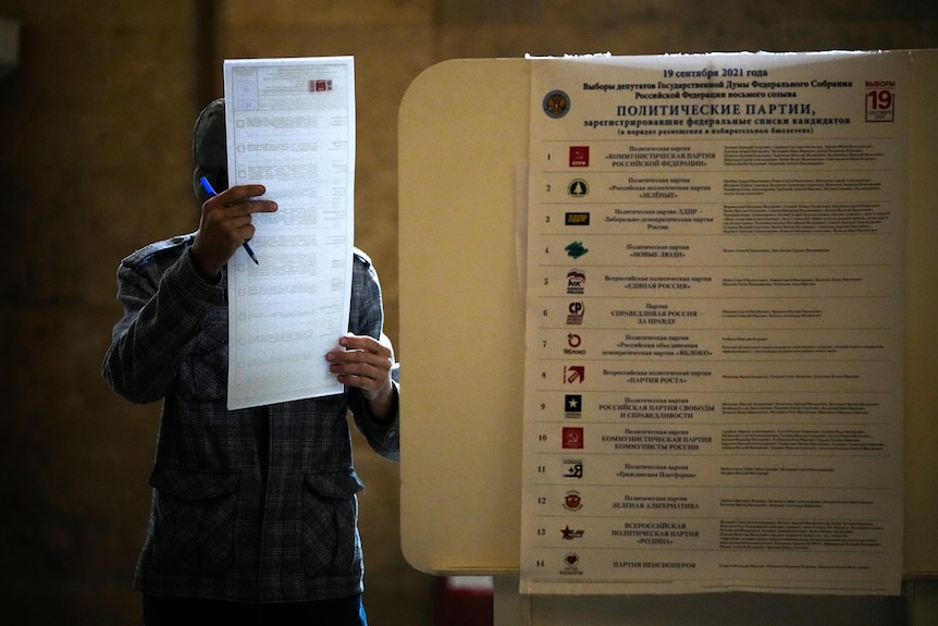 A man reads his ballot at a polling station while holding a blue pen in his right hand.