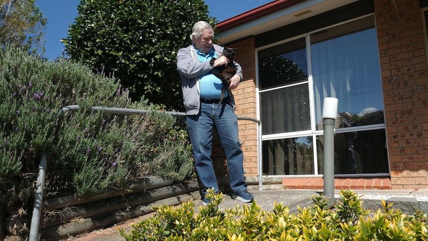 Man stands out the front of his house holding his black cat