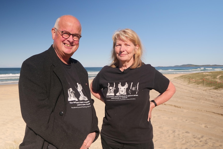 Older man and woman standing on a beach wearing matching black shirts 