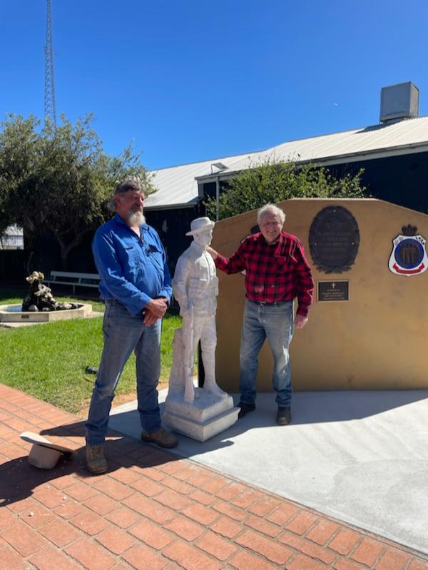 Dois homens estão de cada lado de uma estátua de pedra de um soldado da Primeira Guerra Mundial.
