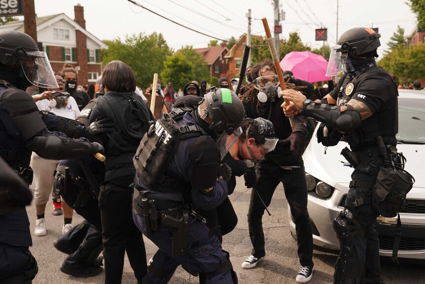 Police holding batons arrest protesters.