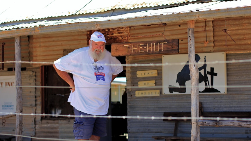 A man stands in front of an old tin building with a sign reading 'the hut'
