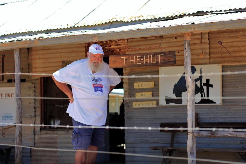 A man stands in front of an old tin building with a sign reading 'the hut'