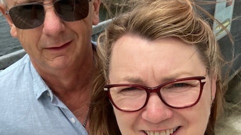 A couple in their 50s smile in a selfie taken on a windy day.