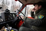 A man with regrowth and and a moustache driving a truck while on the phone