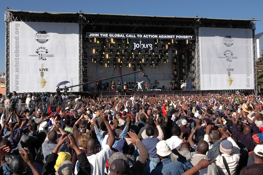 Wideshot of a performer on stage with a large crowd cheering on.
