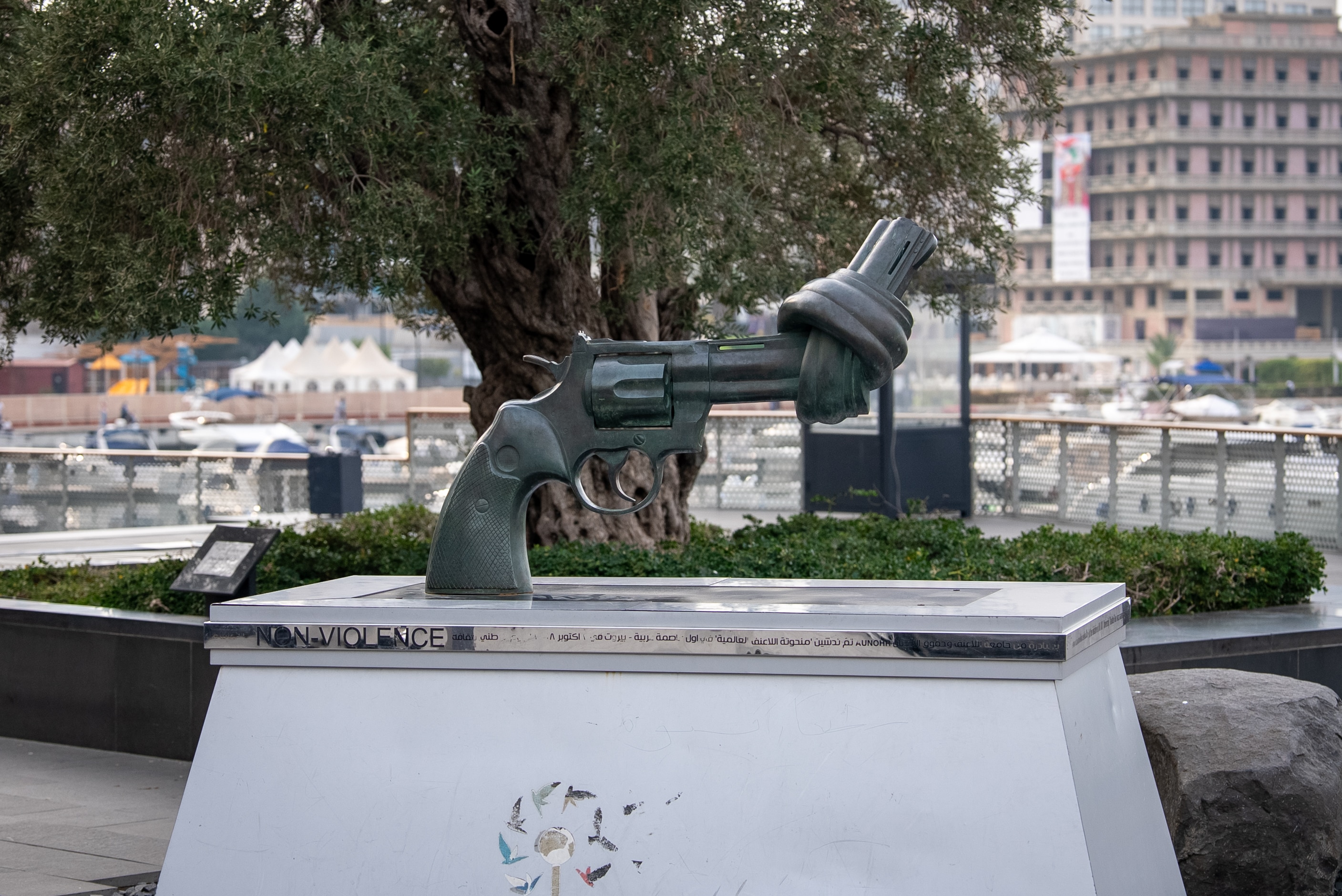 A sculpture in the shape of a gun that has the barrel knotted placed outdoors in a park with the words non-violence underneath