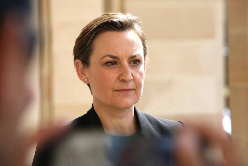 Amber-Jade Sanderson wears a somber expression and a black suit jacket as she waits to address media