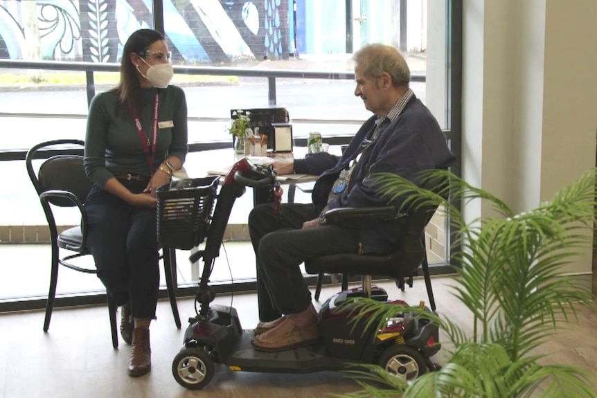 Aged care worker wearing PPE sitting at a table with an aged care resident.