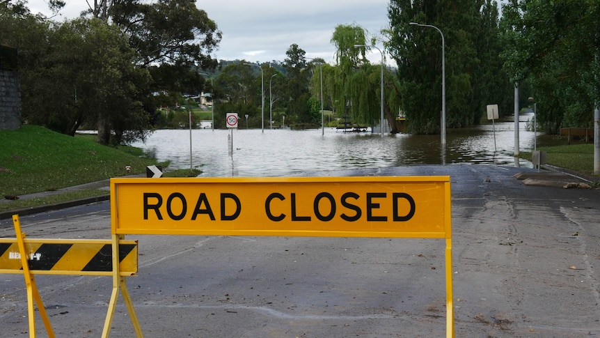 Yellow Road closed sign and barrier to flooded road.