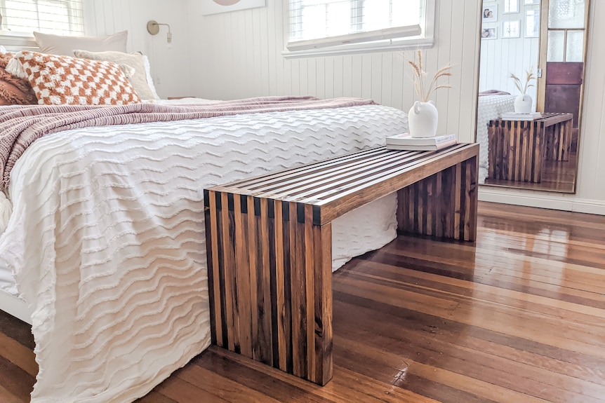 A long wooden bench at the end of a large bed.