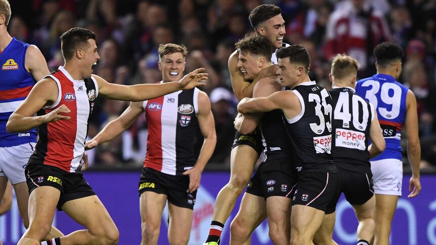 AFL players get around a teammate who has just kicked his first goal.