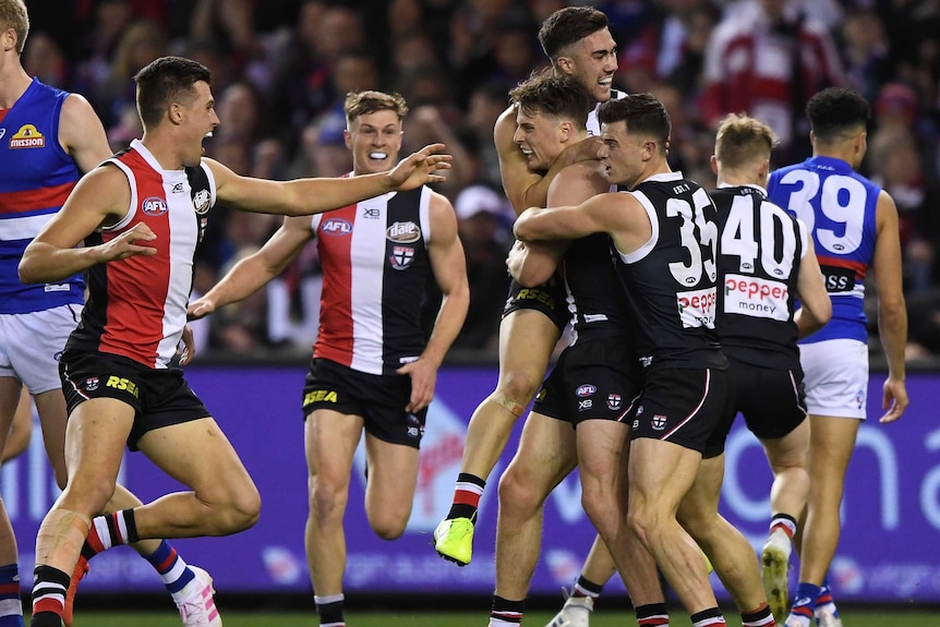 AFL players get around a teammate who has just kicked his first goal.