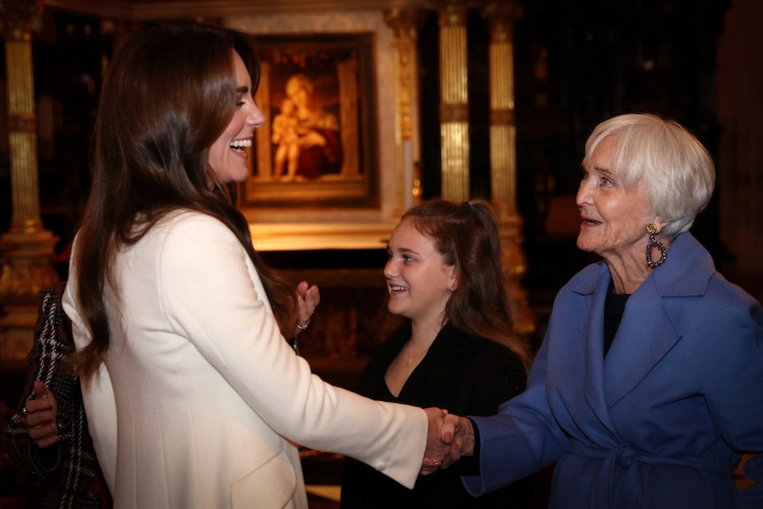 Catherine, Princess of Wales shakes a woman's hand while smiling inside Westminister.