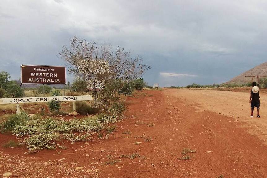 Man walks on a dirt road next to the sign: Welcome to Western Australia