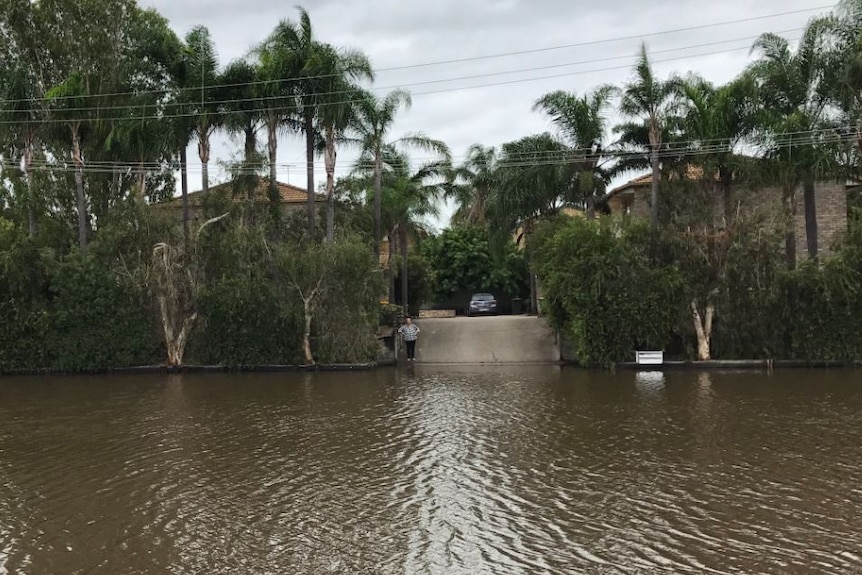 A man stands outside his Beenleigh home as floodwaters cut off his driveway