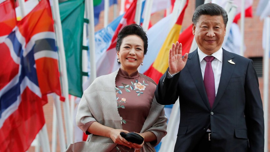 Peng Liyuan, left, and Xi Jinping, right, stand in front of international flags.