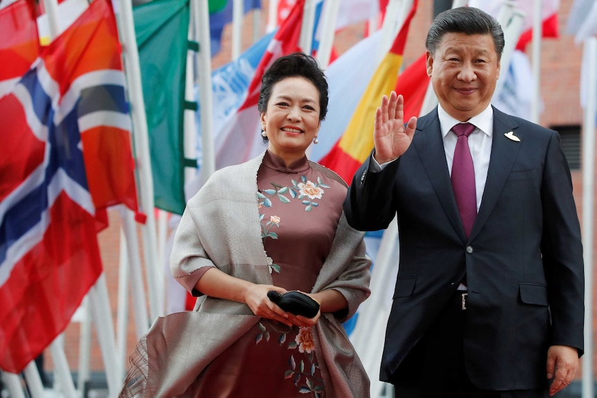 Peng Liyuan, left, and Xi Jinping, right, stand in front of international flags.