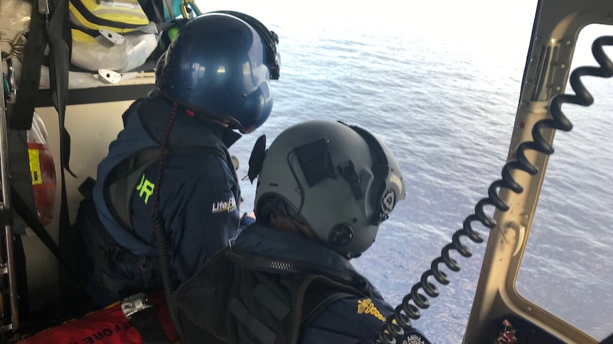 Two Lifelight crew members looking into waters off the side of helicopter.