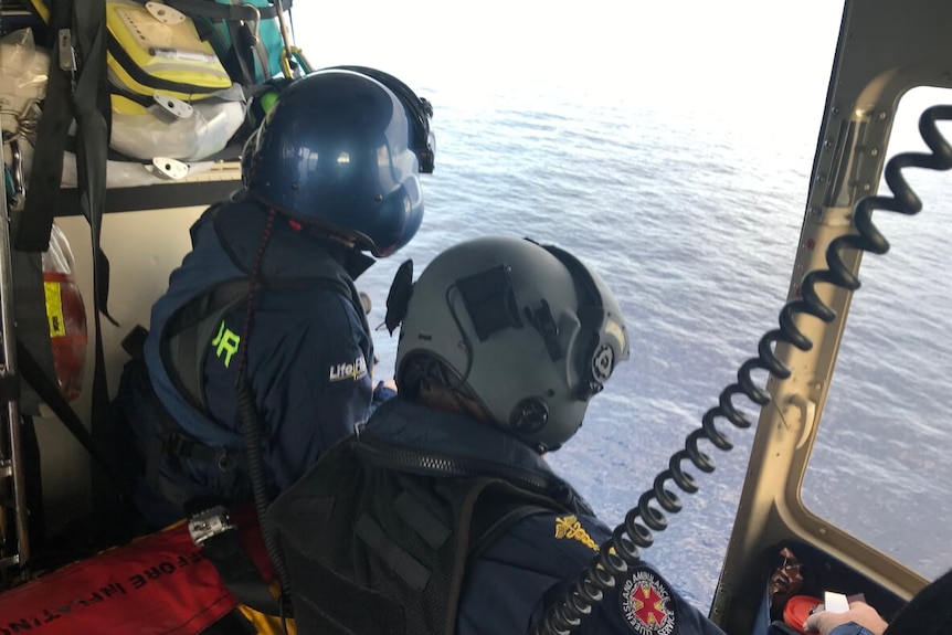 Two Lifelight crew members looking into waters off the side of helicopter.